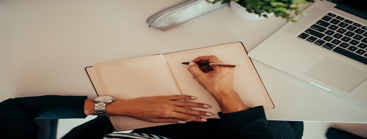 Deftere yazan kişi ve laptop — akademik CV hazırlama