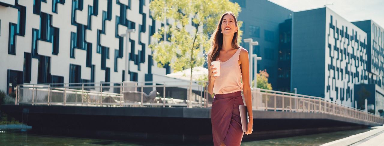 Şık giyimli güzel genç iş kadını kahve ve laptopuyla gülümsüyor