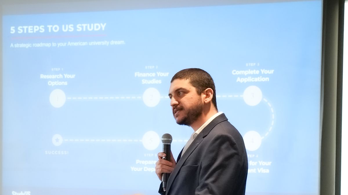 Emre Birol, StudyUS etkinliğinde "5 Steps to US Study" slaytının önünde mikrofonla konuşuyor