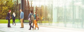 students in front of a modern glass university building